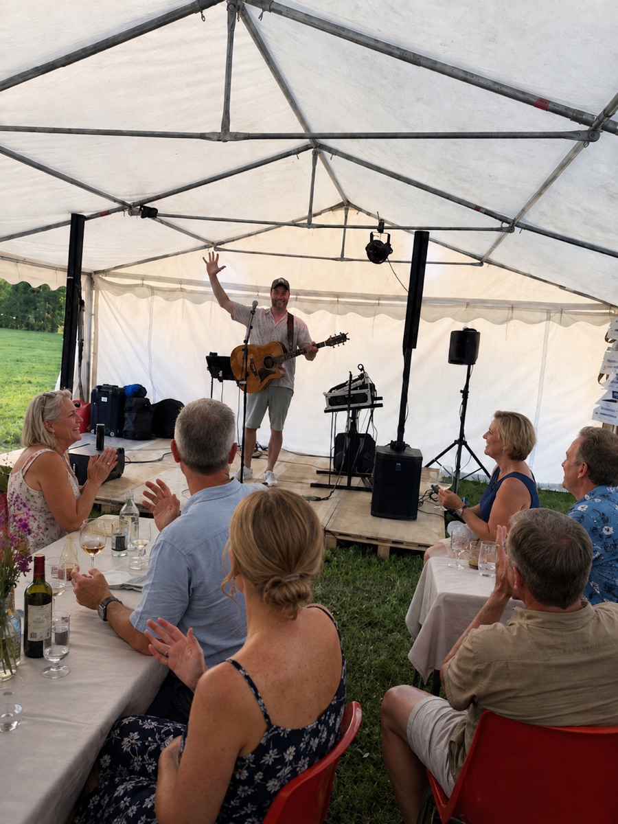 AI-bearbetad stämningsbild: Daniel med gitarr i tältet, med gäster som lyssnar och applåderar vid borden.